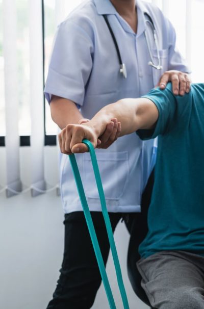 A physiotherapist is helping a patient stretch his arm using cloth at the clinic.