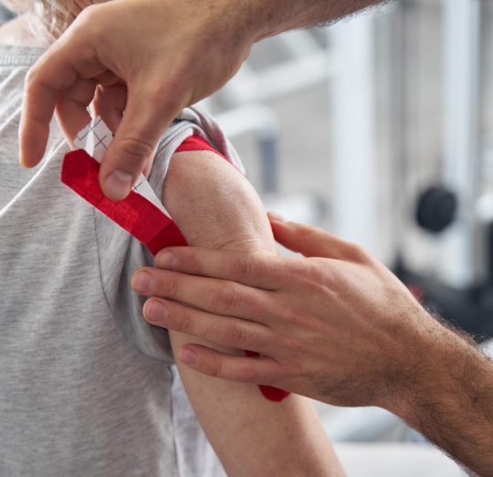male-doctor-putting-red-kinesiology-tape-on-pensio-2022-02-09-23-53-19-utc
